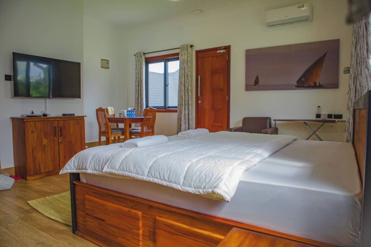 A bedroom with a large bed, wooden furniture, a television, and a painting on the wall.