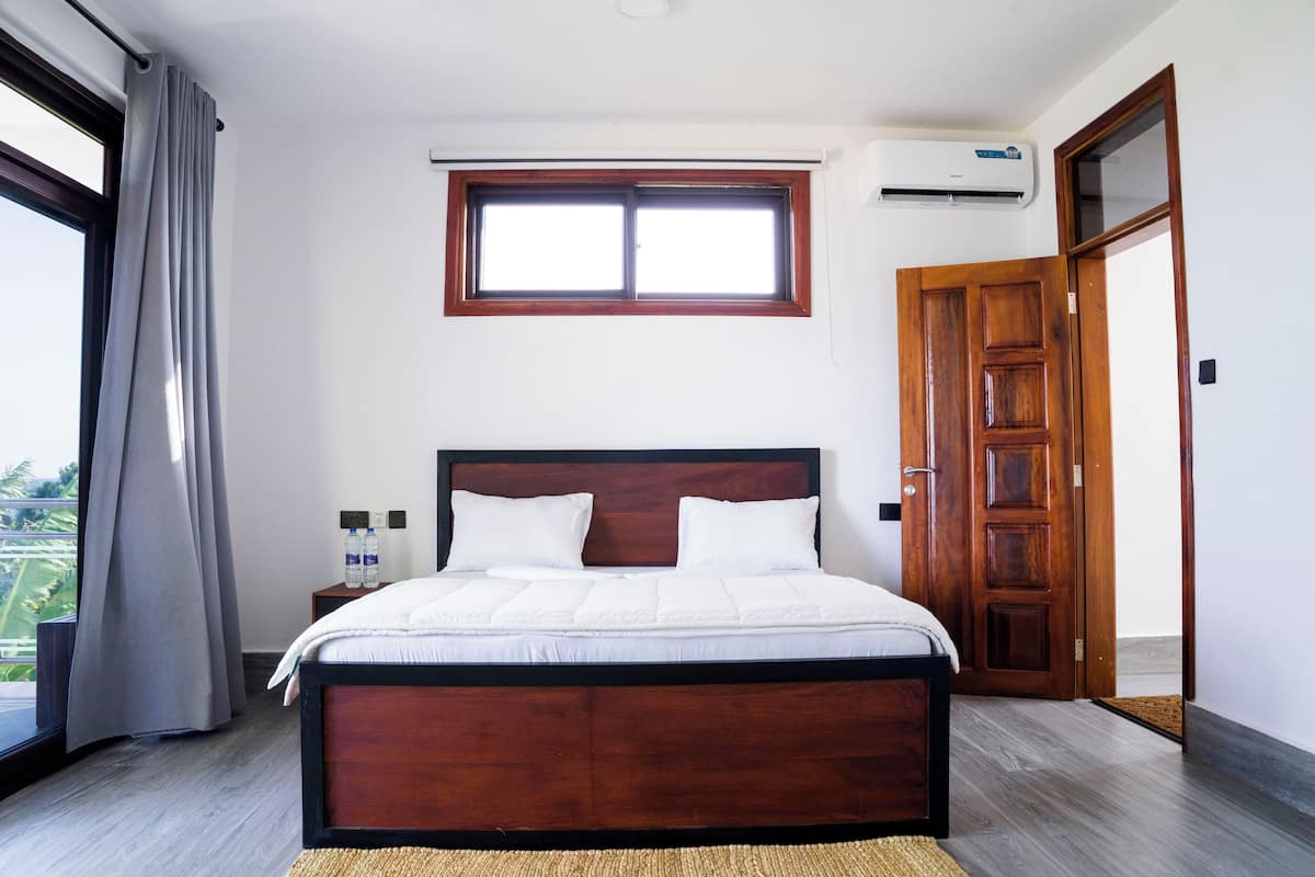 A bedroom with a wooden bed, a window, an air conditioning unit, and a door.