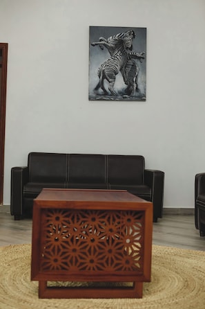 A living room with a black leather sofa, a wooden coffee table with intricate cut-out patterns, and a framed zebra artwork on the wall.