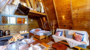 Un accogliente chalet in legno con camera soppalcata, zona pranzo con tavolo apparecchiato per due e soggiorno con divano e poltrone.