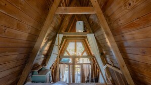 Camera mansardata con travi in legno, un letto, una finestra e un piccolo tavolo.