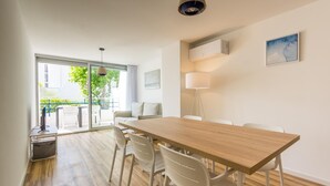 A modern dining area with a wooden table and white chairs, a floor lamp, and a view of the outdoors through a glass door.