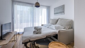A modern hotel room with a bed, a desk, a television, and a large window with sheer curtains.
