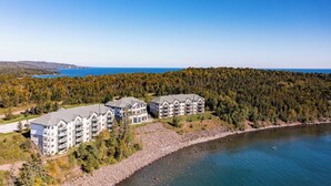 Un hotel de varios pisos con un diseño arquitectónico moderno, ubicado junto a un lago con un paisaje forestal de fondo.