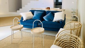 Una sala de estar moderna con un sofá azul, cojines blancos, una mesa de centro y una silla de mimbre.