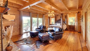 A log cabin interior with a large bed, leather furniture, and a chandelier.