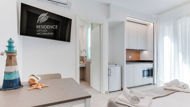 Une chambre d’hôtel moderne dotée d’un coin repas, d’une kitchenette et d’un téléviseur affichant le nom de l’hôtel.