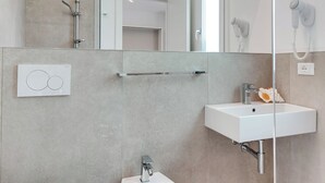 Une salle de bain moderne équipée de toilettes, d’un bidet, d’un lavabo et d’un grand miroir.