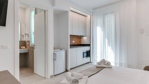 Une chambre d’hôtel moderne équipée d’un lit, d’une petite kitchenette, d’une salle de bain avec douche et d’un téléviseur fixé au mur.