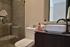 Un baño moderno con cabina de ducha de vidrio, un lavabo blanco con grifo oscuro y un espejo sobre el lavabo.