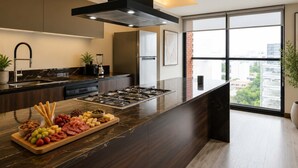 A modern kitchen with a central island, a built-in oven, and a large window offering a city view. - Bright 3BR Apartment | Minutes from Chapultepec (Guadalajara)