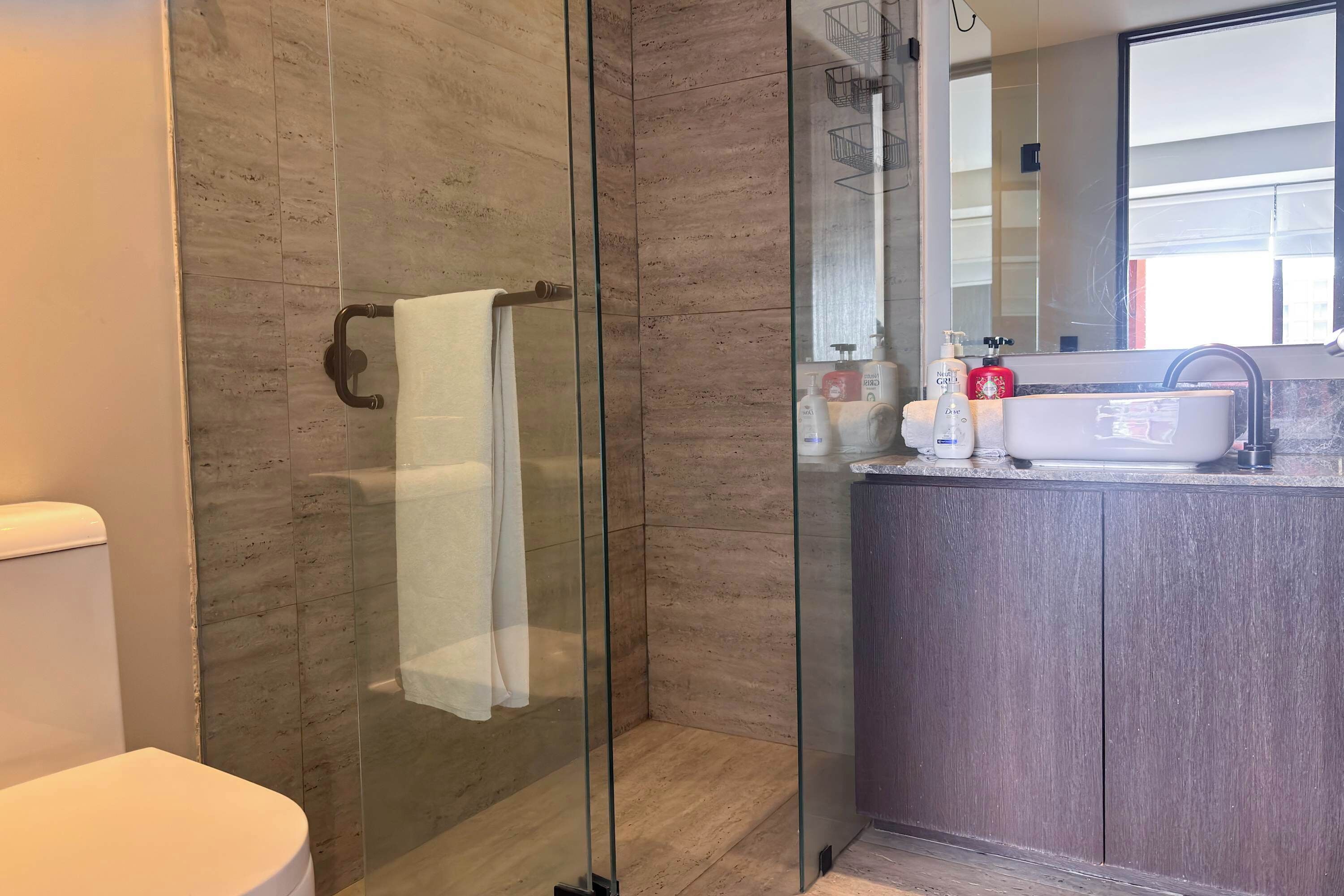 A modern bathroom with a glass shower enclosure, a white toilet, and a vanity with a dark wood finish.