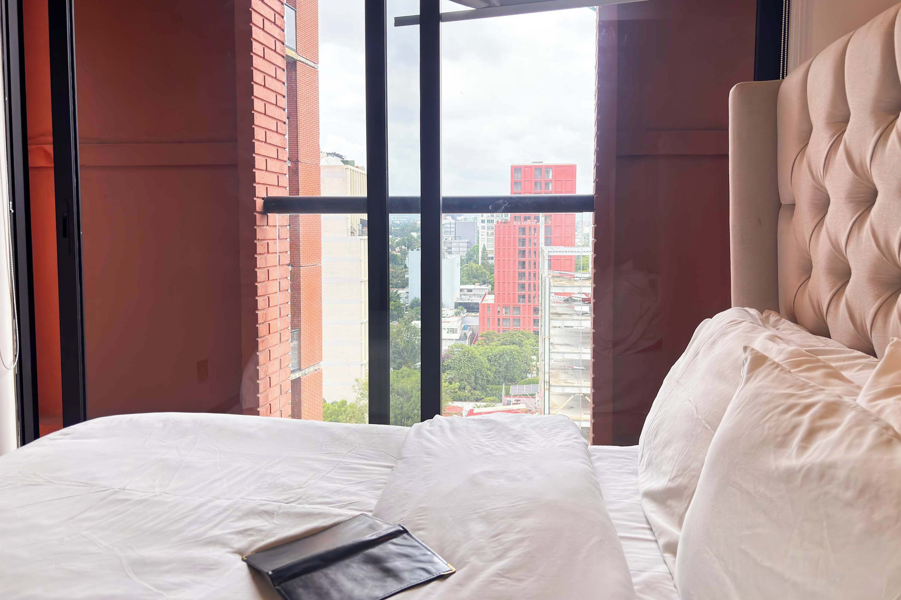 Een hotelkamer met een groot raam, een bed met witte beddengoed en uitzicht op de stadsgezicht.