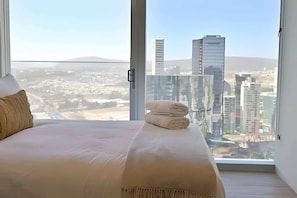Ein Schlafzimmer mit großem Fenster, einem Bett und Blick auf eine Stadtlandschaft.