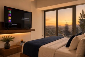 A modern bedroom with a large bed, a TV mounted on a wooden shelf, a bedside table with a plant, and a city view through large windows.