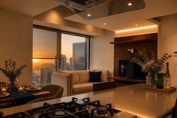 A modern kitchen with a gas stove, a dining area with a table and chairs, a sofa, and a large window with a city view.