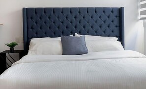 Relax in a serene space with a large bed, tufted headboard, and a potted plant.