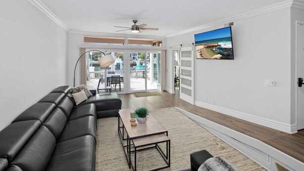 A modern living room with a black leather sectional sofa, a wooden coffee table, and a view of the outdoors through large sliding glass doors. - Coronado On The Strand, Bay or Beach (Coronado)