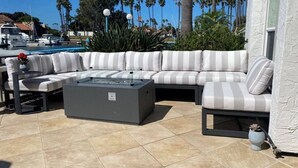 An outdoor seating area with a gray sectional sofa, a small table, and a fire pit. - Coronado On The Strand, Bay or Beach (Coronado)