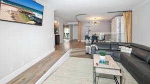 A modern living room with a black leather sofa, a coffee table, and a large painting of a beach scene. - Coronado On The Strand, Bay or Beach (Coronado)