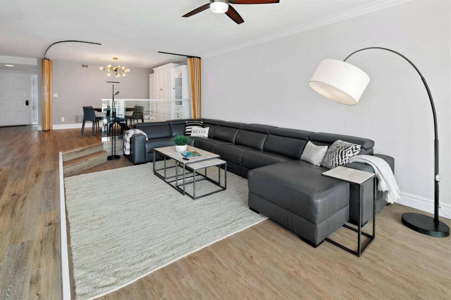 Een moderne woonkamer met een modulaire bank, een salontafel, een vloerlamp en een trap naar een verdieping erboven.