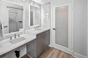 Une salle de bain moderne avec trois lavabos, un grand miroir et une porte en verre dépoli.