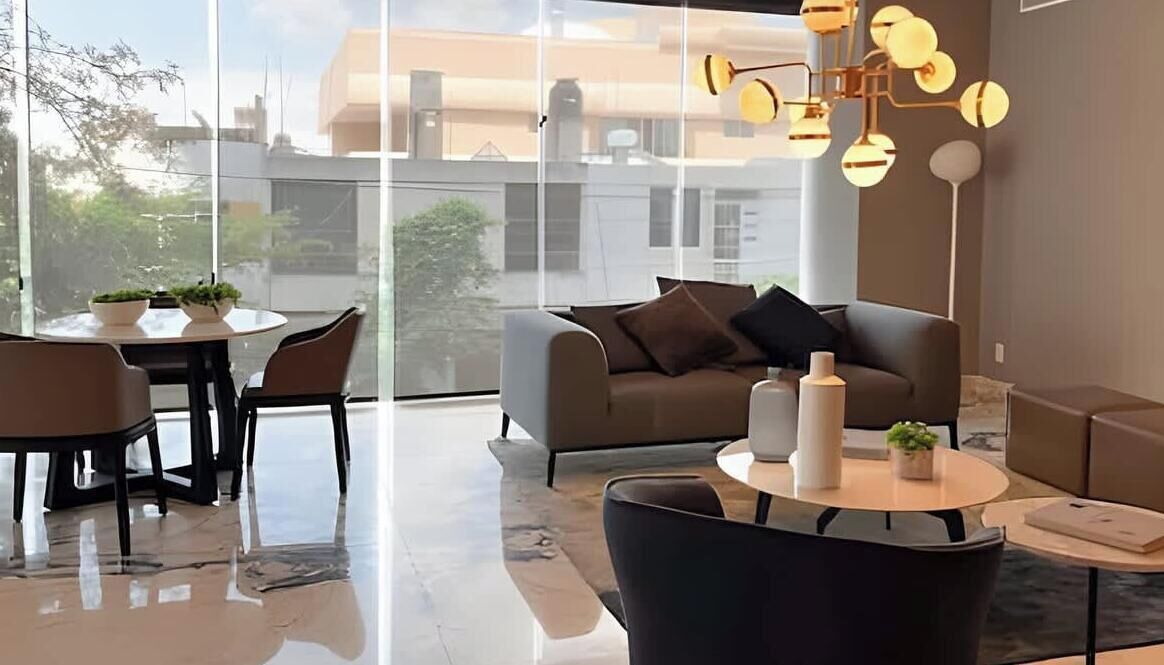 Un salon moderne avec un canapé, une table basse et des fauteuils. Une grande fenêtre offre une vue sur les bâtiments environnants.