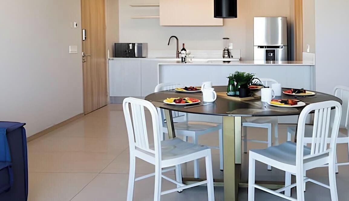 Een moderne keuken met een eettafel voor vier personen, witte stoelen en een klein kookeiland met een plant.
