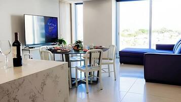 A modern living room with a dining area, a flat-screen TV, and a large window with a view of the outdoors.
