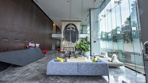 A modern lobby with a reception desk, seating area, and large windows.