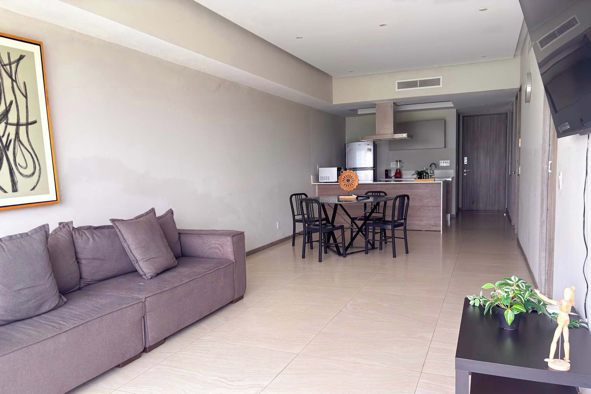 A modern living room with a grey sofa, a dining table with chairs, and a kitchen area in the background.