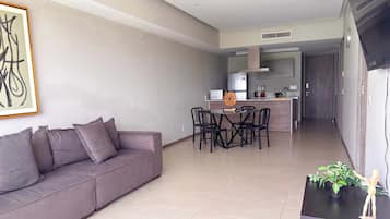 A modern living room with a grey sofa, a dining table with chairs, and a kitchen area in the background.