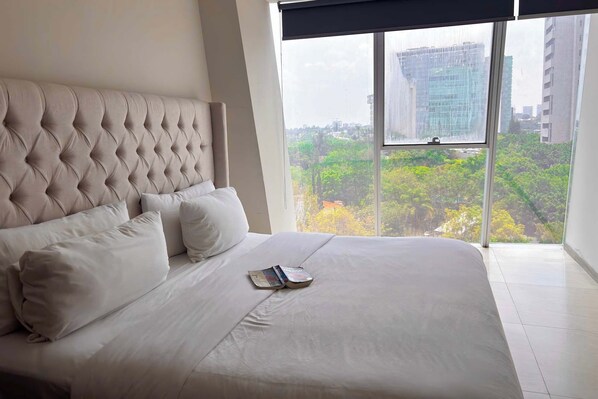 A hotel room with a large bed, a window with a view of buildings and trees, and a modern design.