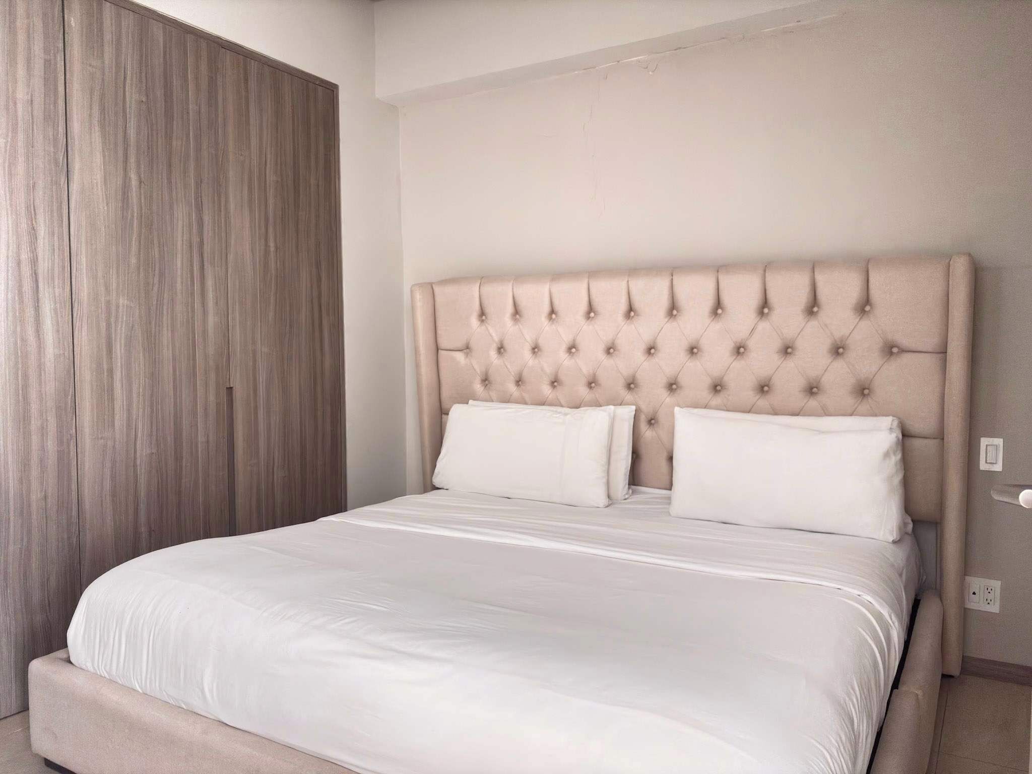 A bed with a tufted headboard, white bedding, and a wooden wardrobe.