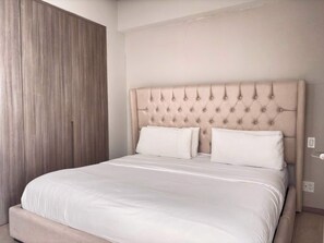 A bed with a tufted headboard, white bedding, and a wooden wardrobe. - Modern Apartment | Luxury, Comfort, and Location (Guadalajara)
