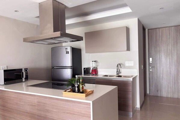 A modern kitchen with a stainless steel refrigerator, a microwave, a blender, and a wooden island with a plant.