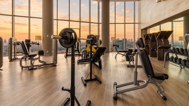 A gym with various exercise equipment, large windows, and a view of the cityscape.