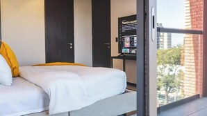 Quarto de hotel com uma cama, uma mesinha de televisão e uma janela com vista para a cidade.