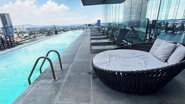 Uma área de piscina no terraço com guarda-corpo de vidro, espreguiçadeiras e vista para a cidade.