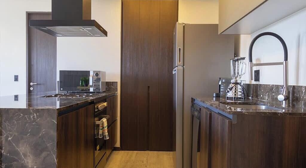 A modern kitchen with a built-in oven, a stainless steel refrigerator, and a wooden door.
