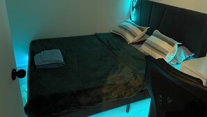 A single bed with a dark headboard, multiple pillows, and a folded towel on the bed.