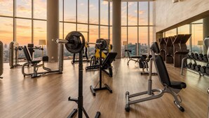 A gym with various exercise equipment, large windows, and a view of the cityscape.