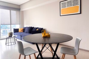 A modern living room with a round table, two chairs, a sofa with cushions, and a large window. - 2BR Near Andares | Stunning City Views (Guadalajara)
