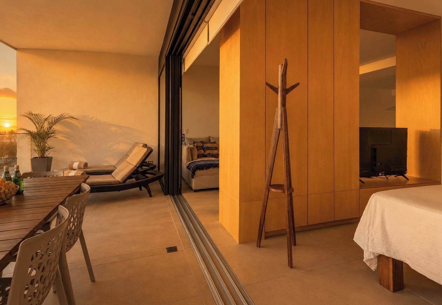 Ein modernes Hotelzimmer mit Bett, Fernseher, einer Holzleiter, einer Couch, einem Esstisch mit Stühlen und einer Topfpflanze.