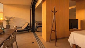 Ein modernes Hotelzimmer mit Bett, Fernseher, einer Holzleiter, einer Couch, einem Esstisch mit Stühlen und einer Topfpflanze.