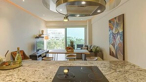 A modern kitchen with a central island, a dining area with a table and chairs, and a large window offering a view of the outdoors.