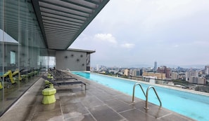 Une piscine sur le toit, dotée de chaises longues et offrant une vue sur la ville.