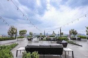 Eine Dachterrasse mit Sitzgelegenheiten im Freien, Lichterketten und Blick auf die Stadt.
