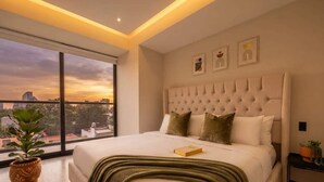 Ein modernes Schlafzimmer mit großem Fenster, einem gepolsterten Kopfteil und Blick auf die Stadt.