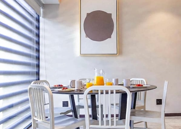 A dining area with a table set for breakfast, including a pitcher of orange juice, a plate of food, and several cups.